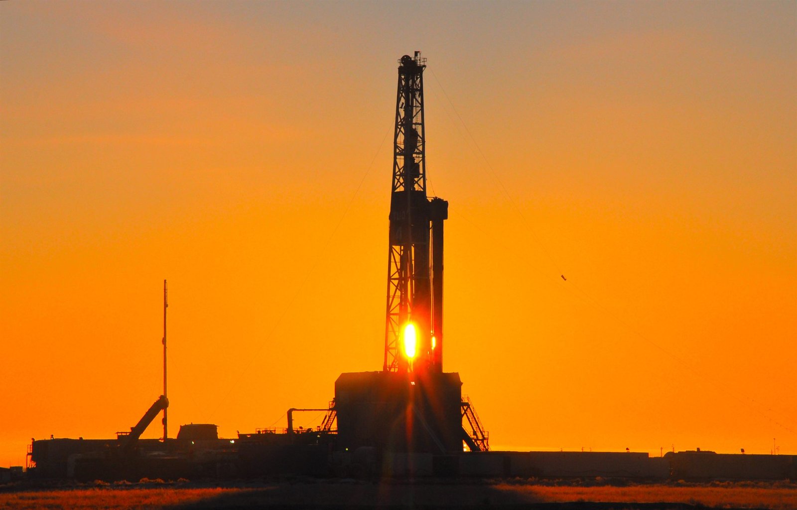 Torre de perforación recortada contra un cielo anaranjado al atardecer